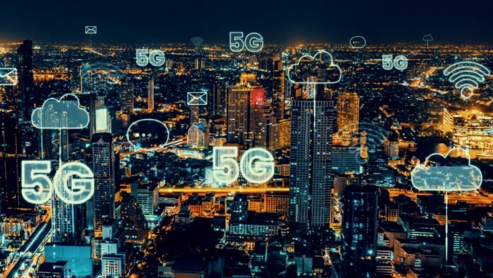 Vista de uma cidade à noite com ícones digitais representando 5G e a Internet das Coisas, simbolizando a conectividade urbana e inovação tecnológica.