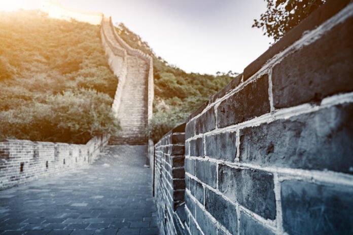 Vista próxima de um trecho da Grande Muralha da China, com degraus subindo em direção ao topo de uma colina coberta de vegetação.