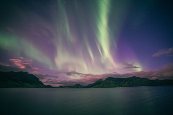 Céu estrelado com auroras boreais em tons de verde e roxo sobre montanhas, refletindo fenômenos astronômicos deslumbrantes.