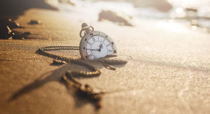 Relógio de bolso na areia ao pôr do sol, simbolizando o conceito de viagem no tempo.