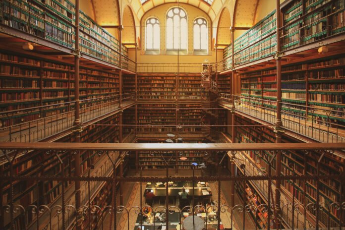 Vista interior de uma biblioteca histórica, com prateleiras repletas de livros e arquitetura clássica.